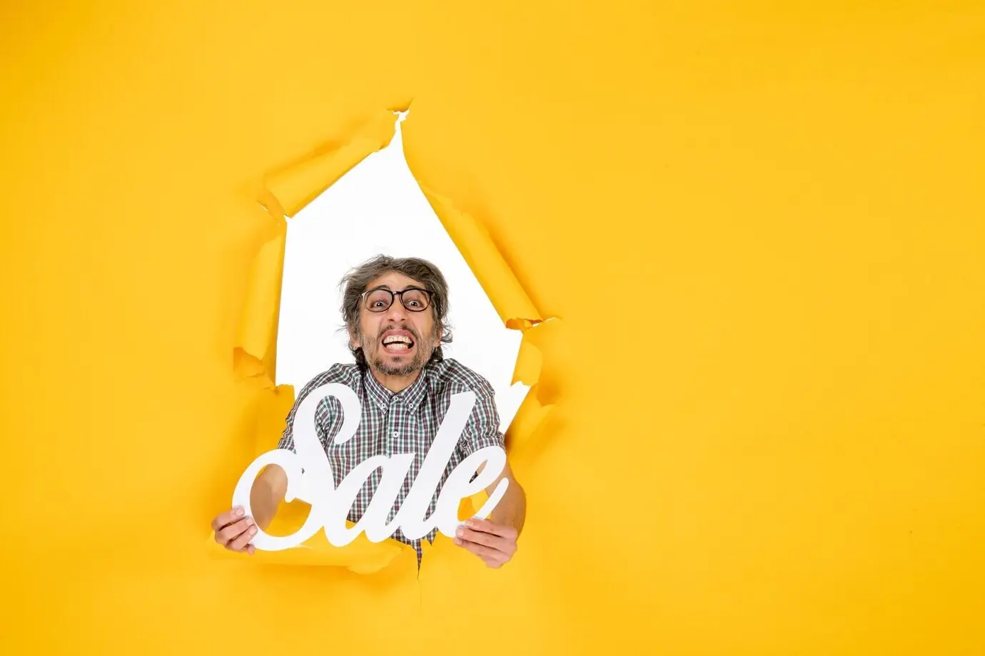 Вид спереди молодого мужчины, держащего белую надпись о распродаже на жёлтой стене.